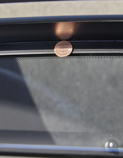 Penny standing upright in window channel to demonstrate flush fitment and tight seal of armored glass in a Mercedes-Maybach SUV.