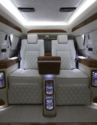 White quilted captain chairs and touchscreen controls in the rear cabin of a Cadillac Escalade VIP conversion by Quality Coachworks.