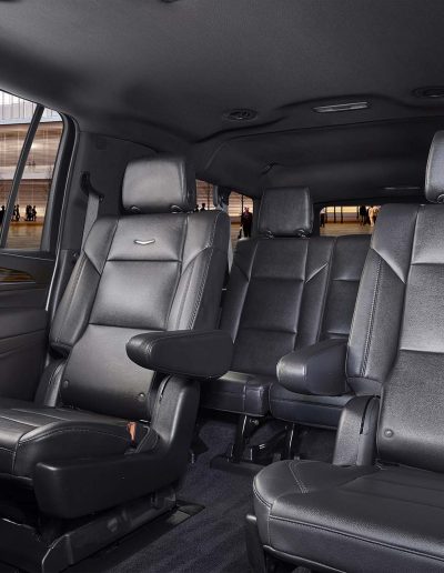 Rear cabin view of a 6-door Cadillac Escalade SUV featuring black leather bench seating and extended legroom for VIP travel.