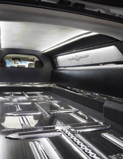 Interior view of the casket bay in a Lincoln Nautilus hearse conversion, featuring chrome rollers and custom trim by Quality Coachworks.