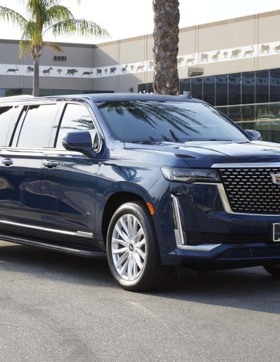 Front angle of a blue 6-door Cadillac Escalade parked in Southern California, converted by Quality Coachworks for high-end transport.