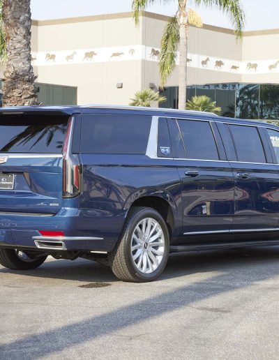 Rear exterior view of a blue 6-door Cadillac Escalade SUV parked outside Quality Coachworks, highlighting extended body styling.