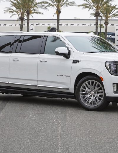 Side view of a white 6-door GMC Yukon Denali SUV with extended body, built for VIP or group travel by Quality Coachworks