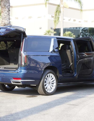Rear and side doors open on a blue 6-door SUV Cadillac Escalade SUV conversion by Quality Coachworks, showing extended cabin access.