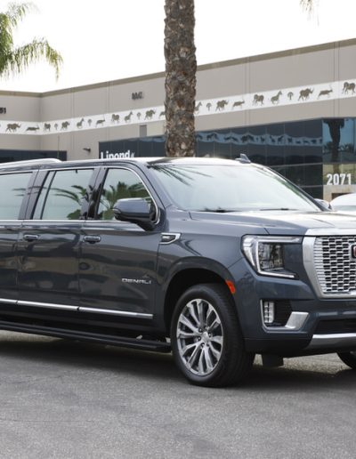 Three-quarter front view of a grey 6-door GMC Yukon Denali SUV parked outside Quality Coachworks.
