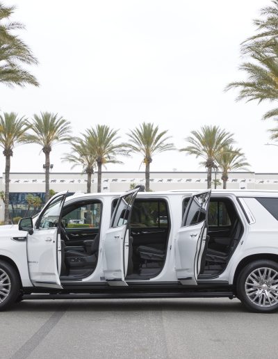 Side view of a white 6-door GMC Yukon Denali SUV with all six doors open, displaying extended body access and custom interior by Quality Coachworks.