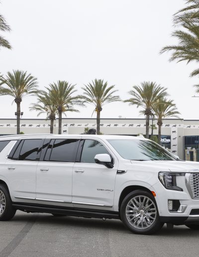 Angled front view of a white 6-door GMC Yukon Denali SUV with chrome grille and extended doors, built by Quality Coachworks.