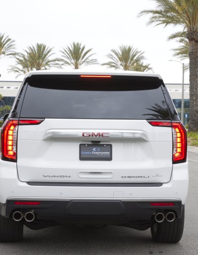 Rear view of a white 6-door GMC Yukon Denali SUV conversion with tinted windows and chrome accents, custom-built by Quality Coachworks.