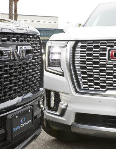 Close-up of two GMC Yukon Denali grilles — black and chrome — showing side-by-side comparison of custom 6-door SUV conversions by Quality Coachworks.