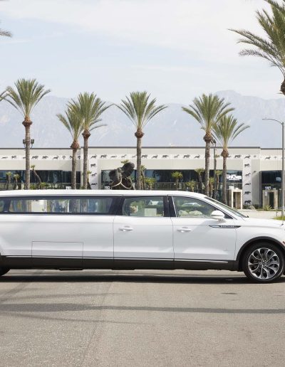 Side profile of a white Lincoln Nautilus 6-door hearse parked outside Quality Coachworks, custom-built for funeral transportation.