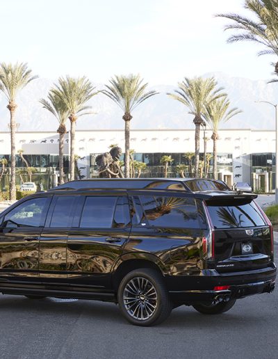 Rear angle of a Cadillac Escalade SUV conversion parked in front of palm trees, custom-built for luxury transport by Quality Coachworks.