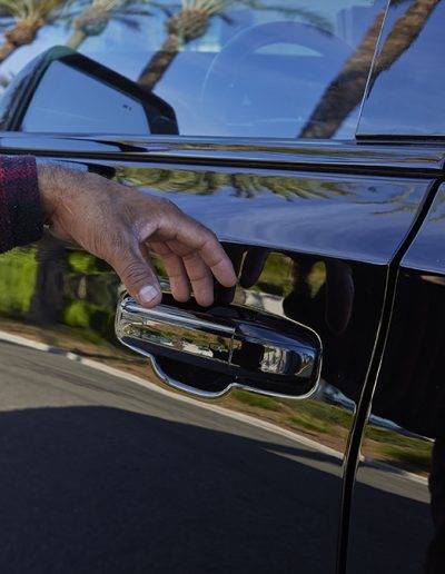 Close-up of a hand opening the chrome door handle on a black Cadillac Escalade SUV, custom-built by Quality Coachworks. Electric SHock doorhandles.