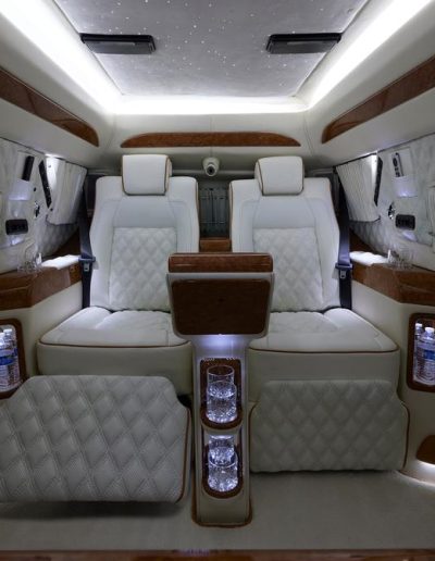 Luxury interior of a Cadillac Escalade 6-door SUV featuring white quilted leather seats, ambient lighting, and wood accents.
