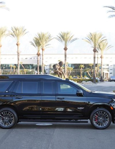 "Side profile of a black Cadillac Escalade SUV conversion by Quality Coachworks, parked in front of palm trees