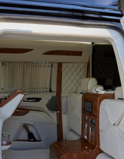 Custom luxury cabin inside a Cadillac Escalade, designed with wood cabinetry, white leather seating, and full privacy curtains by Quality Coachworks.