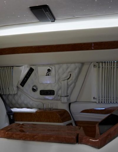 Interior view of a luxury Cadillac Escalade conversion featuring wood trim, LED ambient lighting, and quilted privacy drapes
