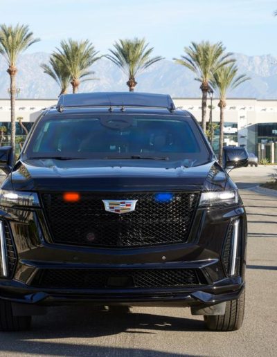 Front view of a black armored Cadillac Escalade with emergency lights, custom-built by Quality Coachworks for security and executive protection.