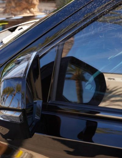 Side mirror of a black armored SUV with visible ballistic window layering and reinforced door, built by Quality Coachworks.