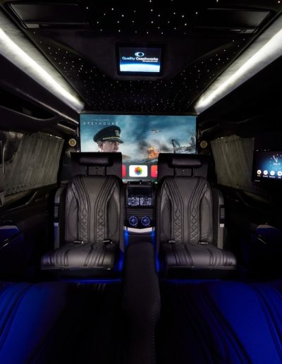 Rear cabin view of a Cadillac Escalade custom interior with dual captain seats, ambient lighting, and full entertainment system.