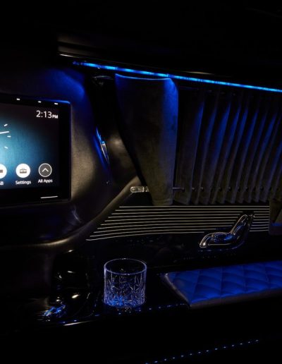 Touchscreen control panel and premium cupholder area inside a Quality Coachworks custom Cadillac Escalade interior with blue LED lighting.